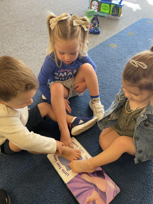 Three preschool children exploring their hands and feet